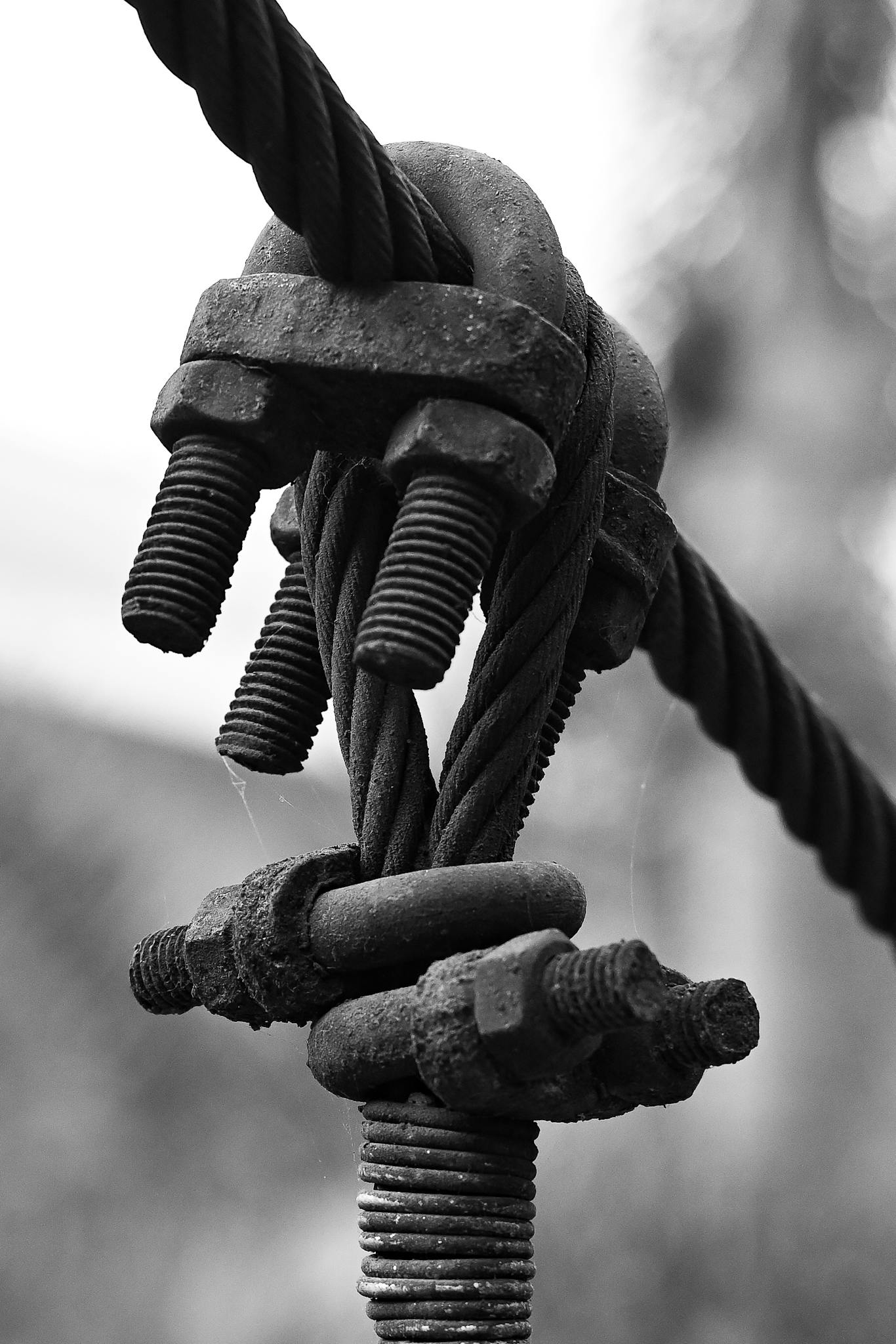 Black and white close-up of a cable tension system with bolts and rust detailing.