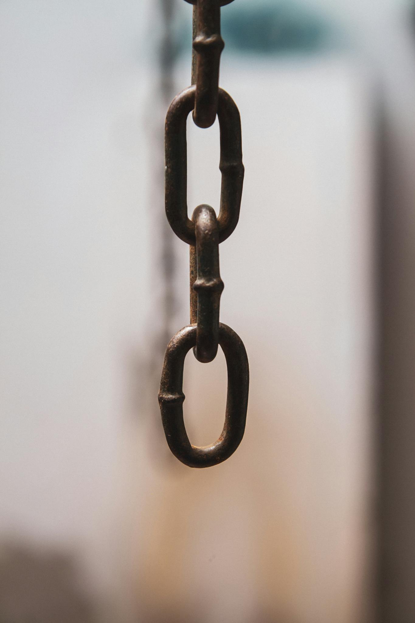 Detailed view of an iron chain link hanging vertically with a soft focus background.