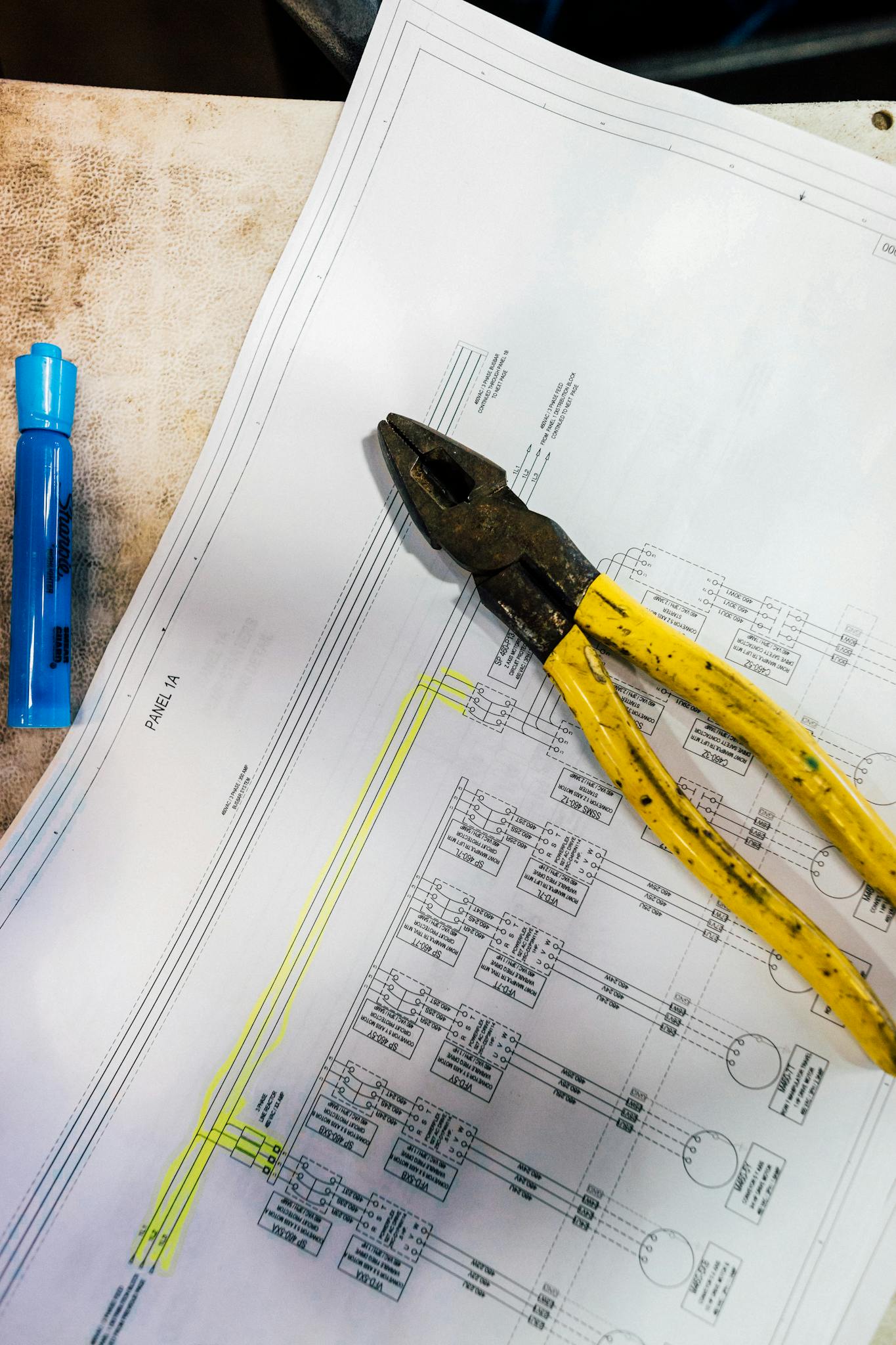 Overhead view of a workshop table with pliers and blueprint for an electrical project.